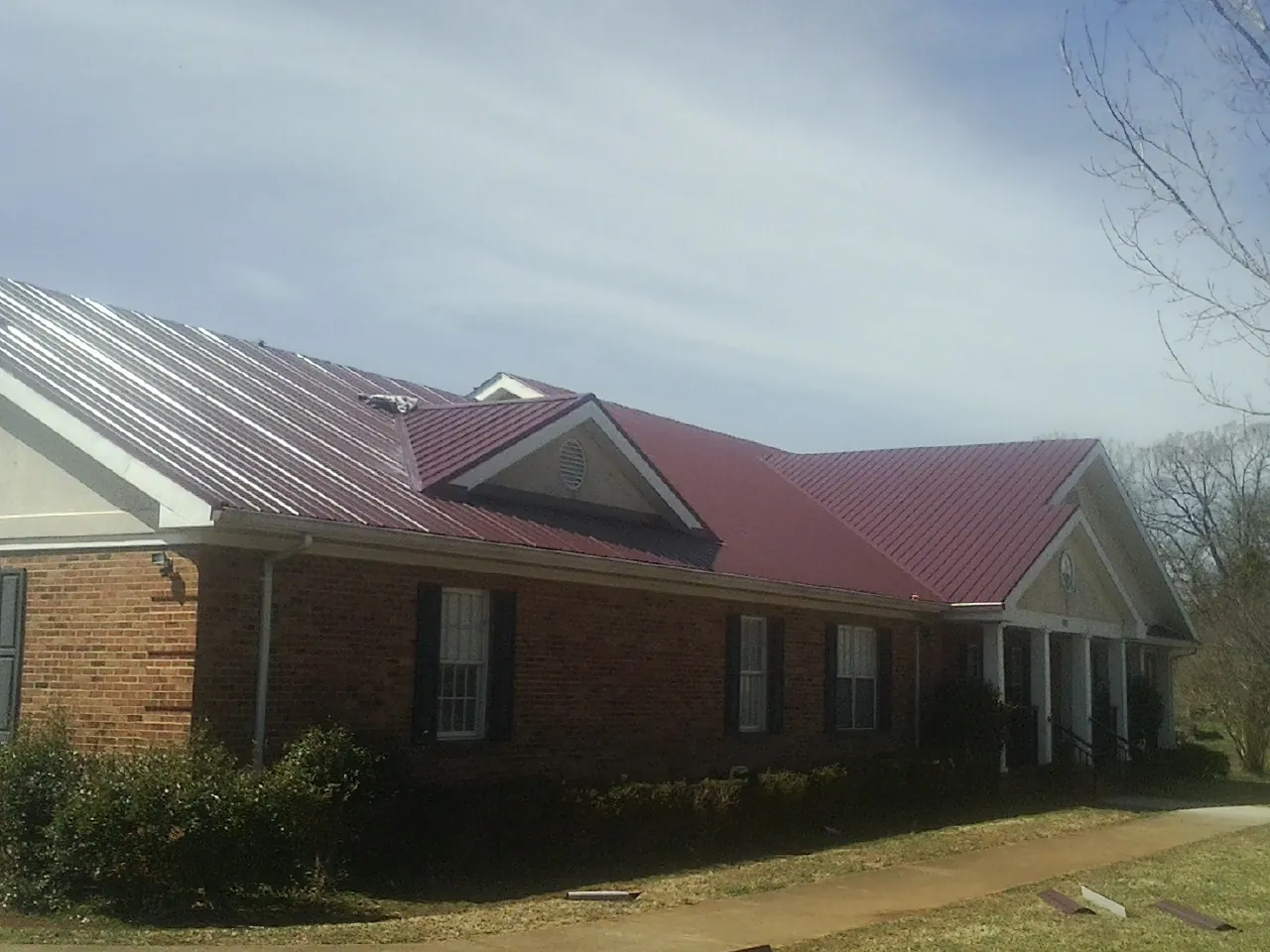 Red metal roof with gabled entries on a long brick building, from a Hail Damage Roof Repair job in Mars