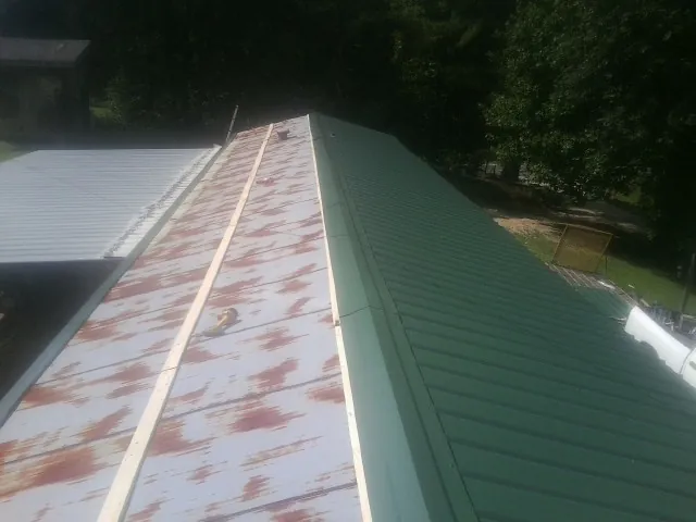 Old rusted panels beside newly installed green metal roofing — Wind Damage Roof Repair by Roofing Brothers in Mars