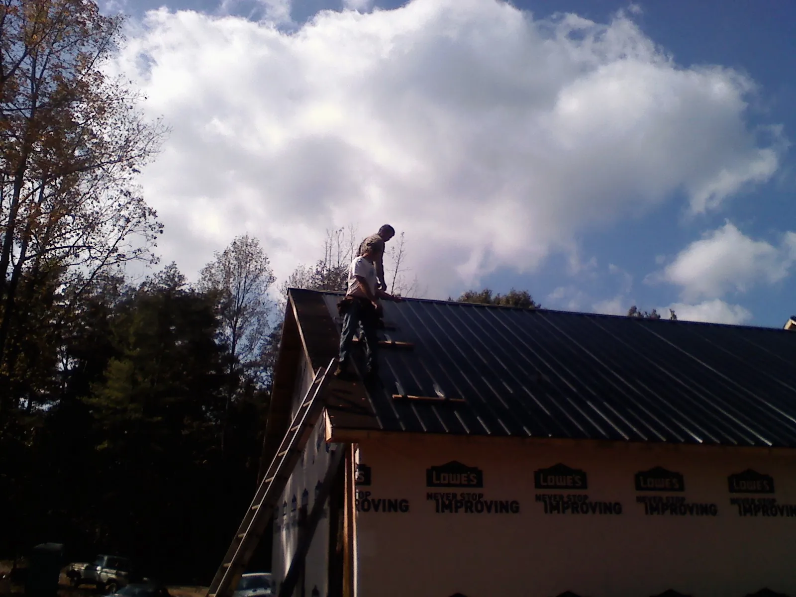 Roofer fastening dark metal panels high against a cloudy sky, from a Roof Inspection job in Mars